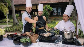 Un chef preparando comida al aire libre con una parrilla, utensilios de cocina y varios recipientes.