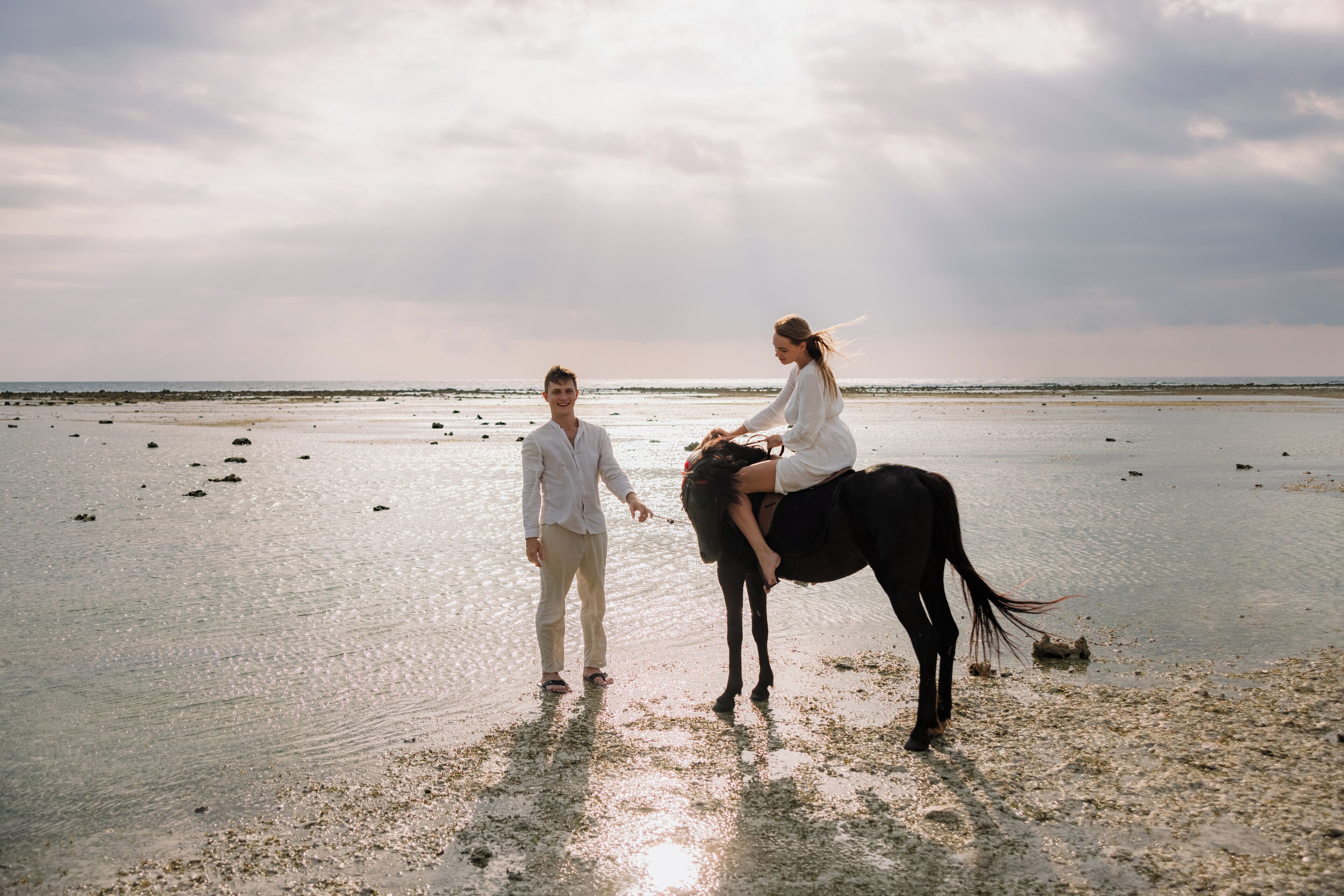 Una pareja en la playa caminando por la orilla con un caballo.