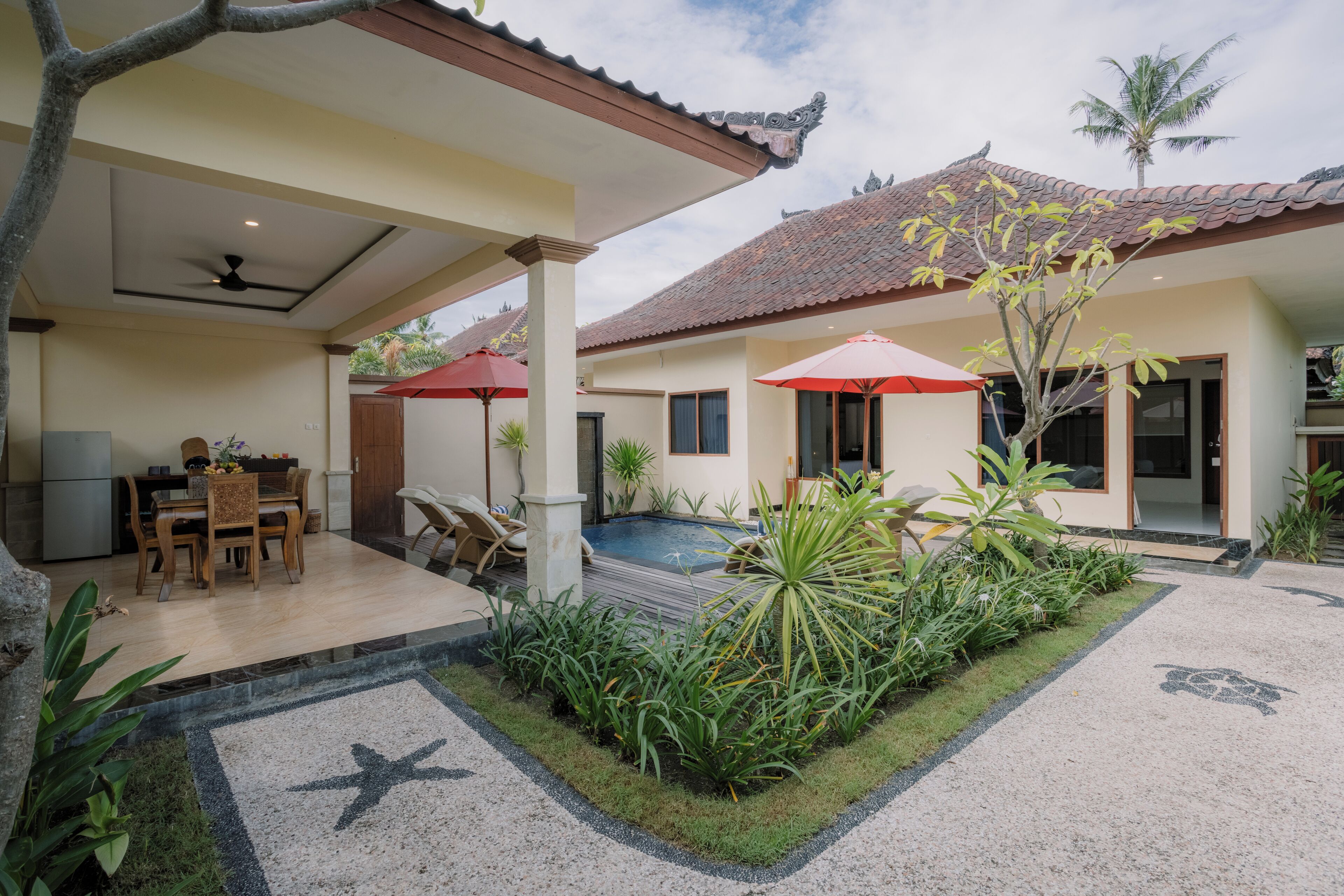 A covered outdoor area with a pool, dining table, and chairs, surrounded by plants and a starfish-patterned floor.