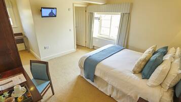 A hotel room with a bed, a desk with a tray of breakfast items, a TV on the wall, and a window with curtains.