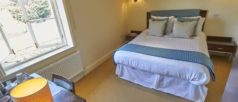A bedroom with a bed, bedside tables, a desk with a lamp, a window, and a radiator.
