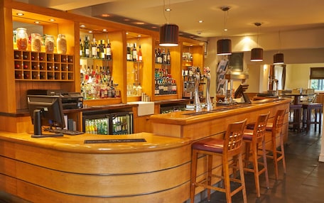 A bar area with a curved wooden counter, bar stools, and shelves stocked with bottles.