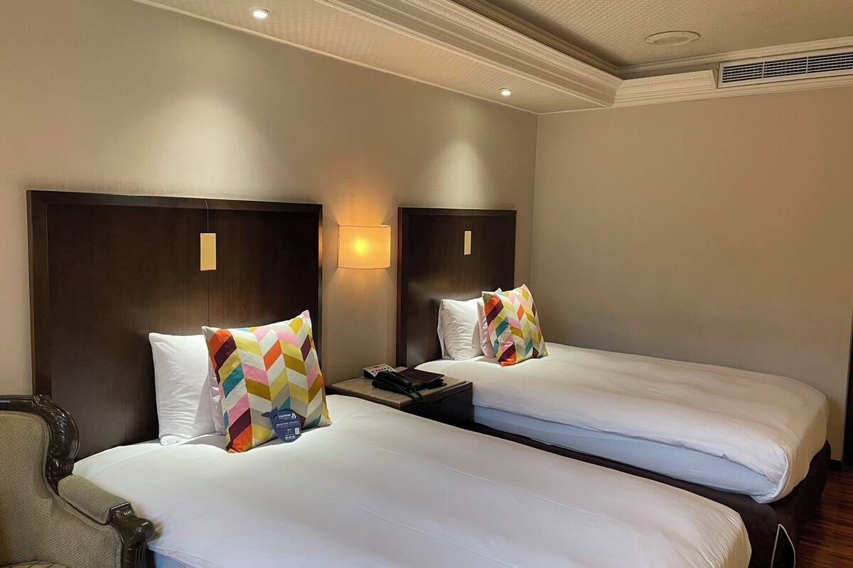 A hotel room with two single beds, each with a wooden headboard and a bedside table.