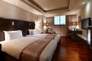 A hotel room with two large beds, a desk, a chair, a television, and a large window with curtains.