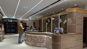 Een hotel receptie met een gebogen marmeren balie, een digitaal scherm en een tijdschriftrek.