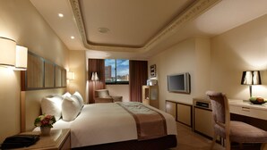 Een hotelkamer met een groot bed, een bureau, een stoel, een televisie en een raam met uitzicht op de stad.