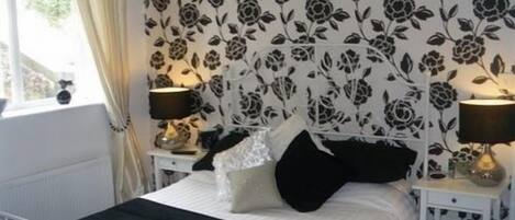 A bedroom with a bed, two bedside tables, a window with curtains, and a floral wallpaper pattern.