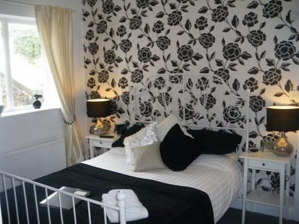 Une chambre à coucher avec un lit, deux tables de chevet, une fenêtre avec des rideaux et un papier peint à motifs floraux.