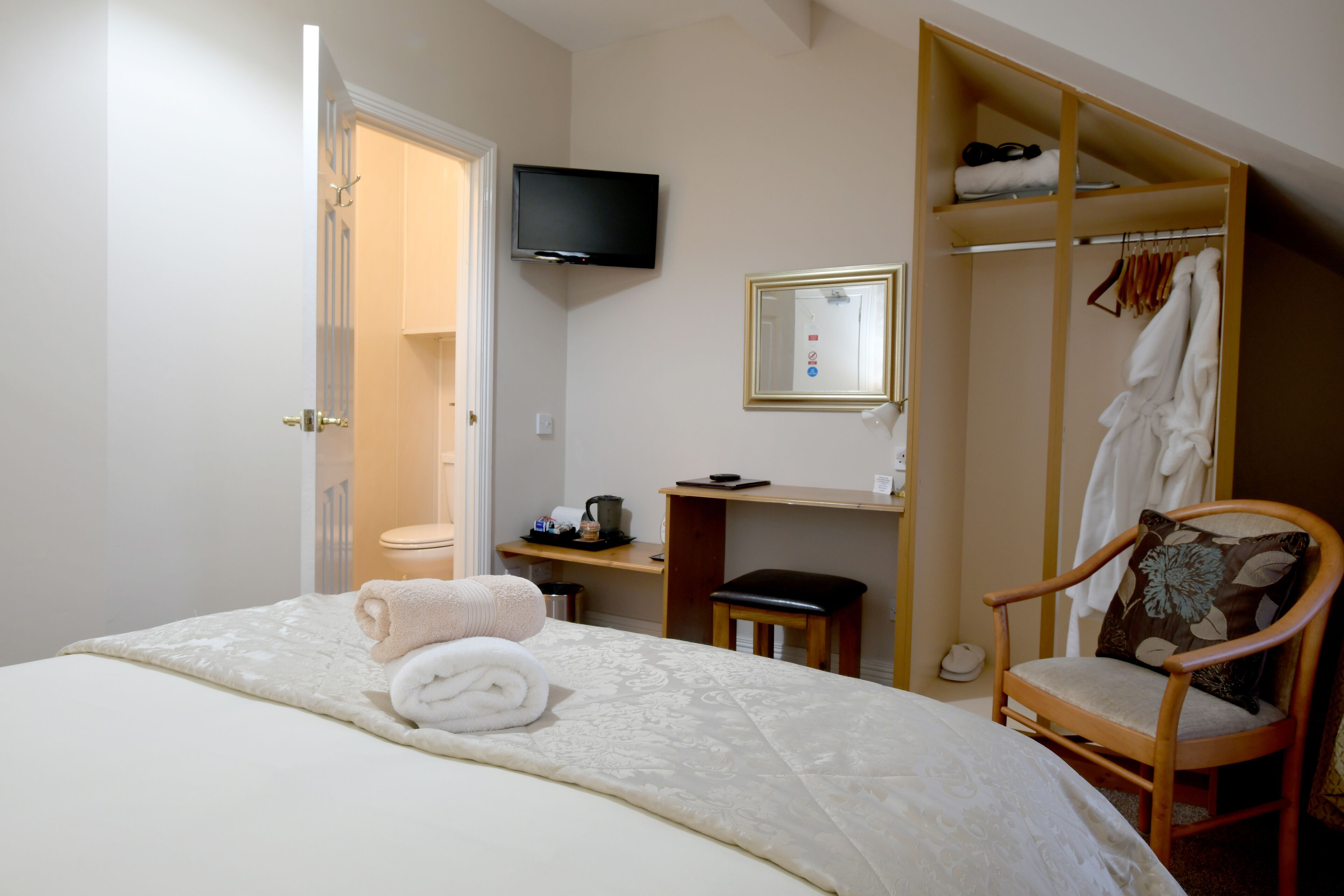 A bedroom with a bed, a chair, a TV, a mirror, and a wardrobe.
