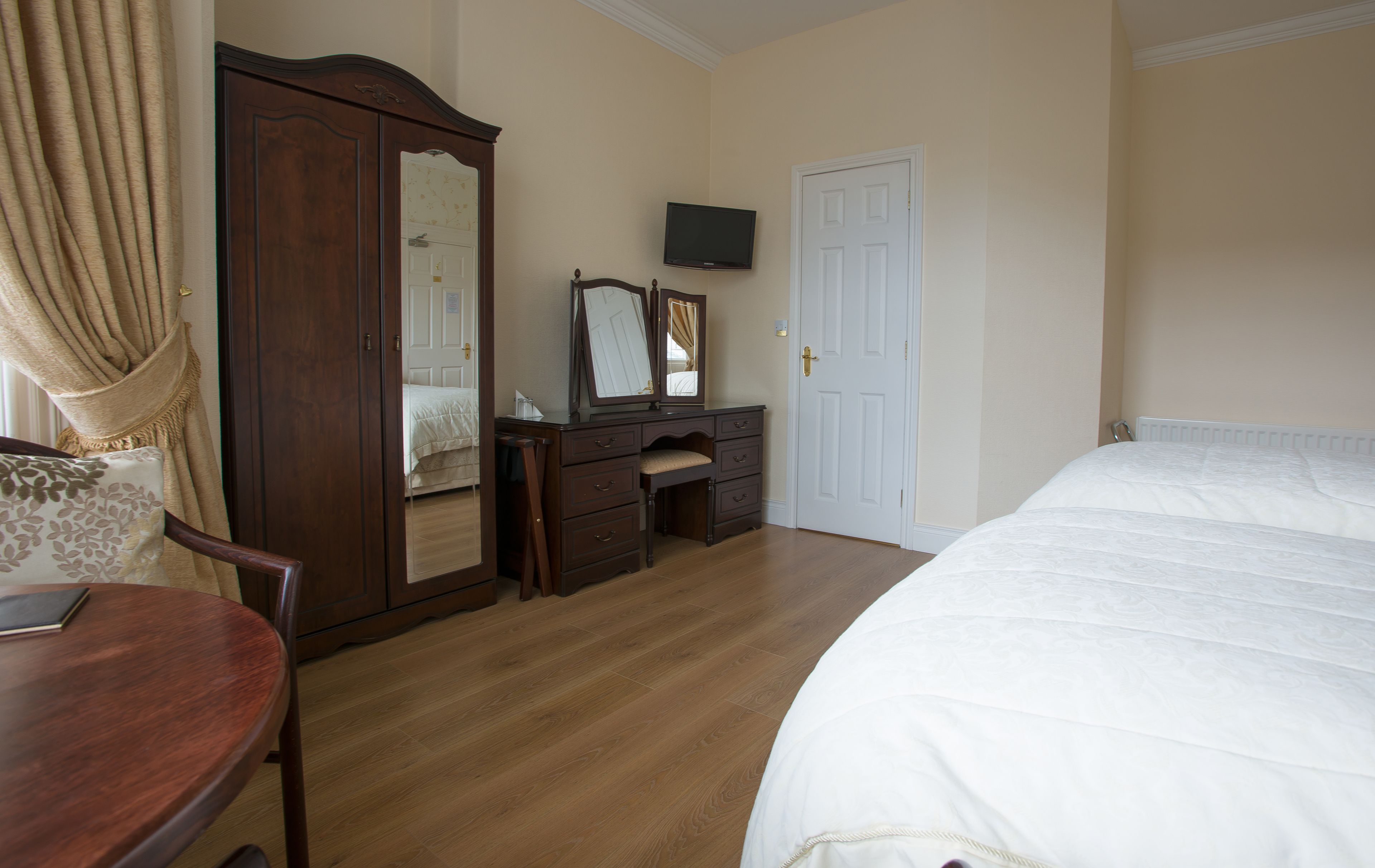 Un dormitorio con una cama, un aparador con espejo, una televisión y una puerta.