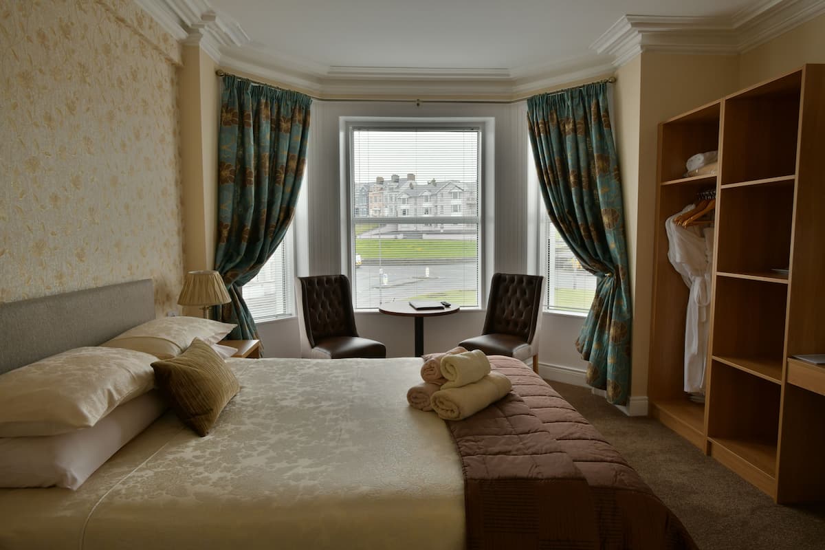 Habitación de hotel con una cama grande, un área de descanso con dos sillas, una mesita y vista a un edificio a través de una ventana.