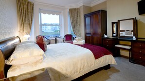 A hotel room with a large bed, a desk, a chair, a wardrobe, and a window with curtains.