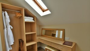 A bedroom with a wooden wardrobe, a desk with a mirror, and a skylight.