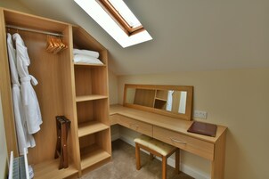 Quarto com guarda-roupa de madeira, escrivaninha com espelho e claraboia.