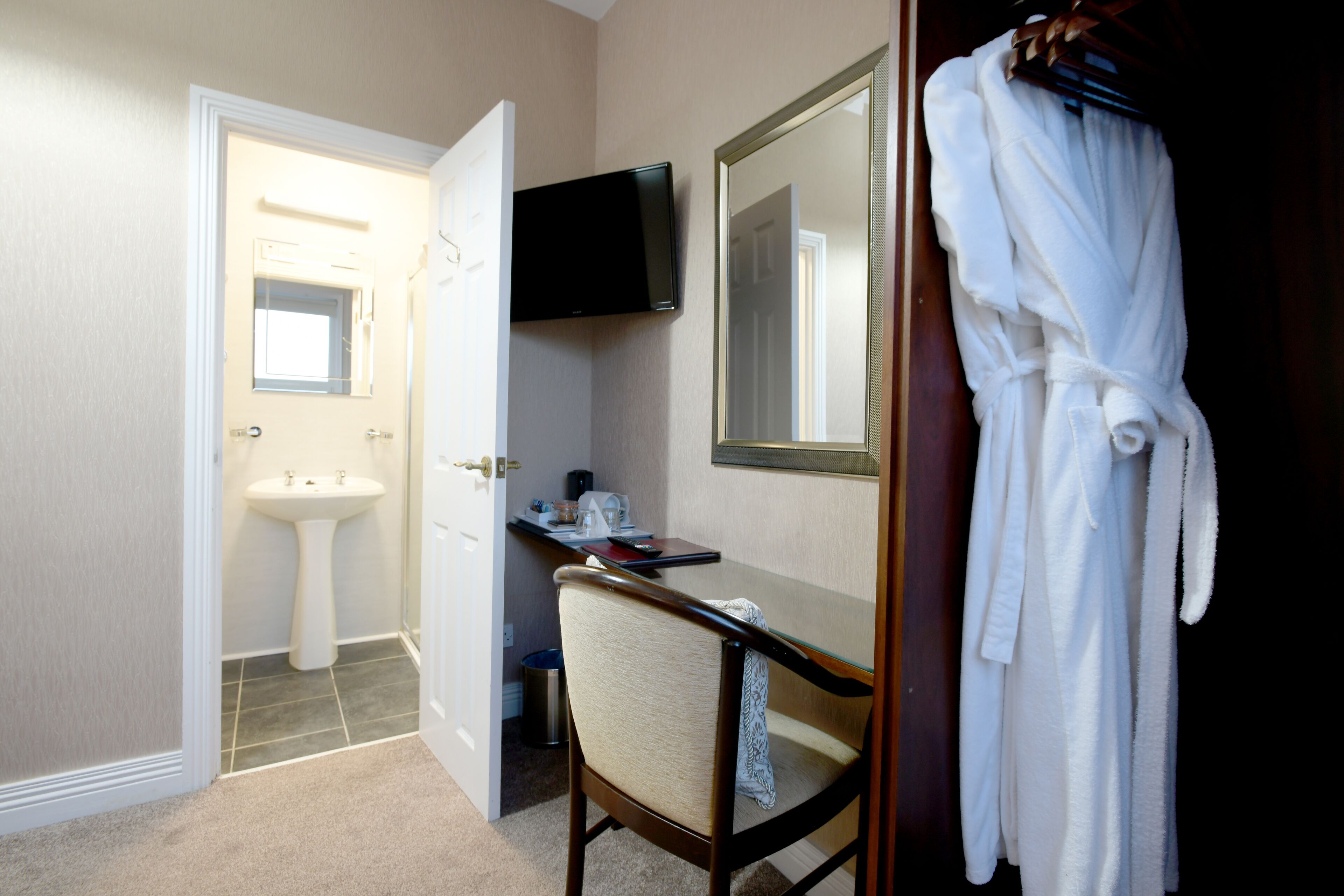 A hotel bathroom with a sink, mirror, robe rack, and a flat-screen TV.