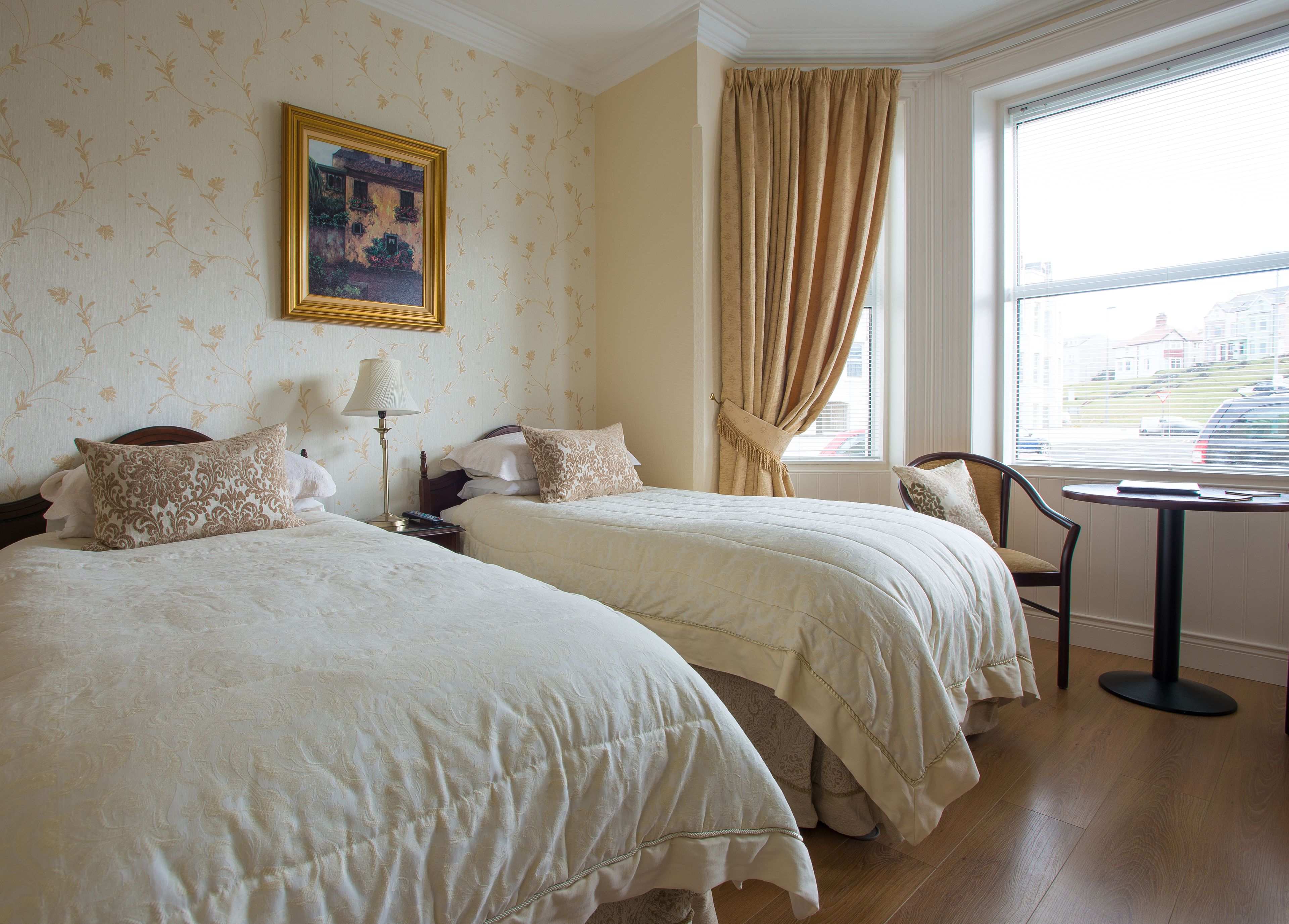 Une chambre d’hôtel avec deux lits, une table de chevet, une lampe, une chaise et une fenêtre avec des rideaux.