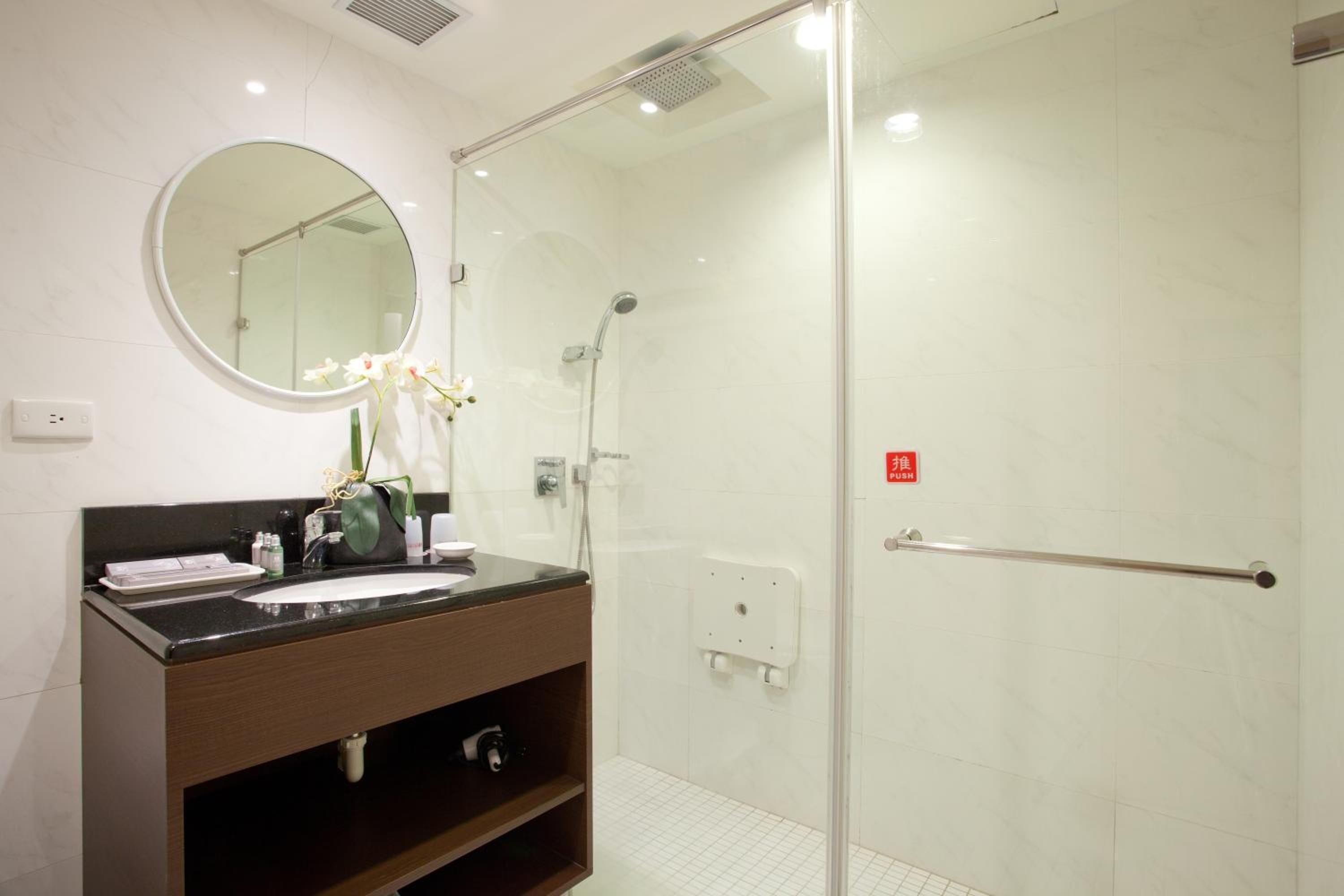 A modern bathroom with a glass-enclosed shower, a round mirror, and a dark wooden vanity.