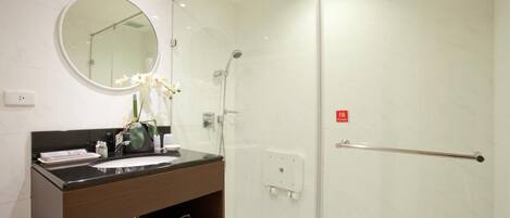 A modern bathroom with a glass-enclosed shower, a round mirror, and a dark wooden vanity.