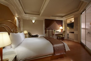 A hotel room with a large bed, a desk, a chair, and a television.