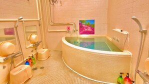 A bathroom with a large bathtub, a shower, and a toilet. There are colorful bottles on the floor. - Hotel Hoshi Kai Kan (Tokyo)