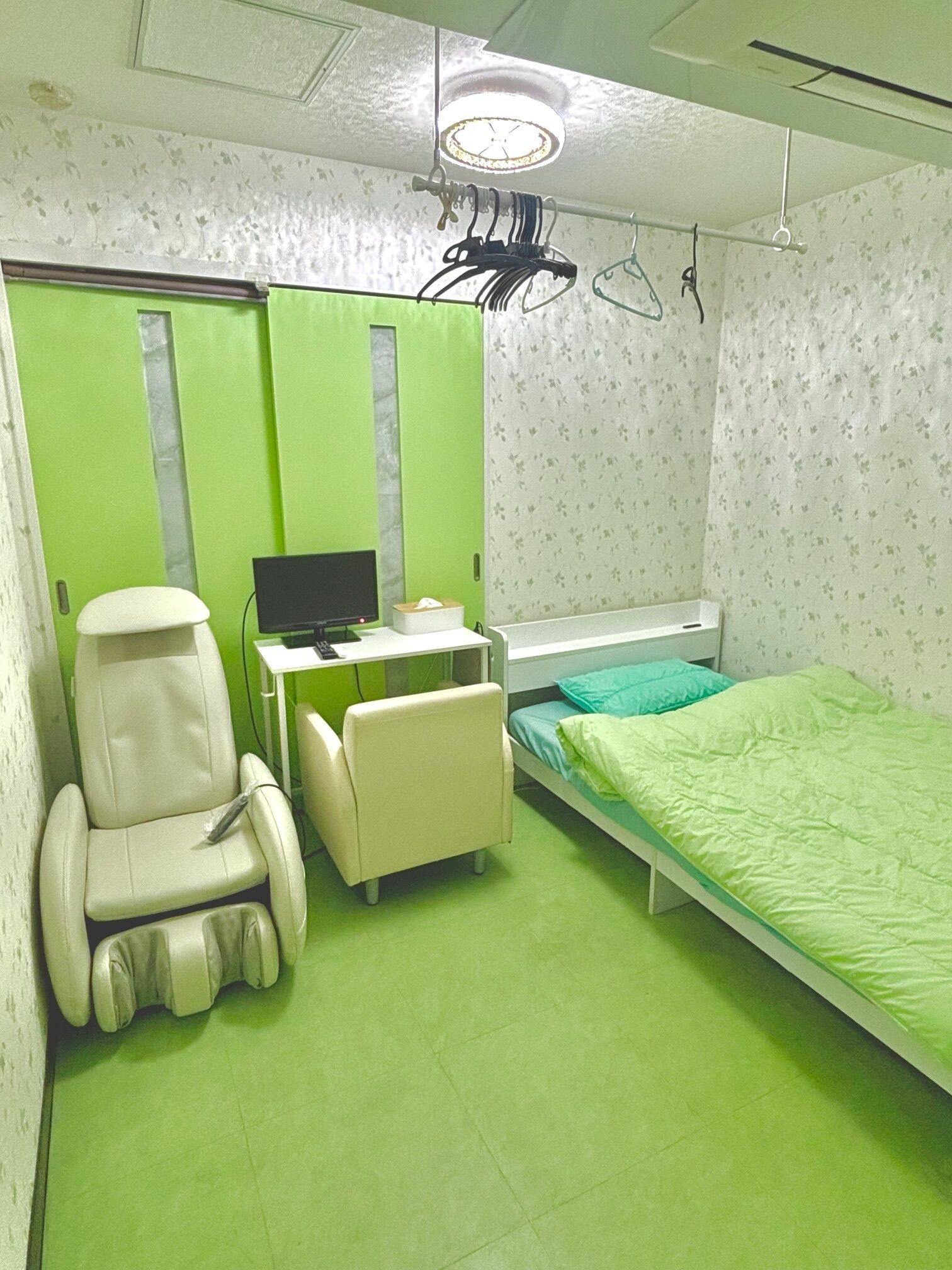 A small, private room with a bed, a desk with a computer, a chair, and a footrest.