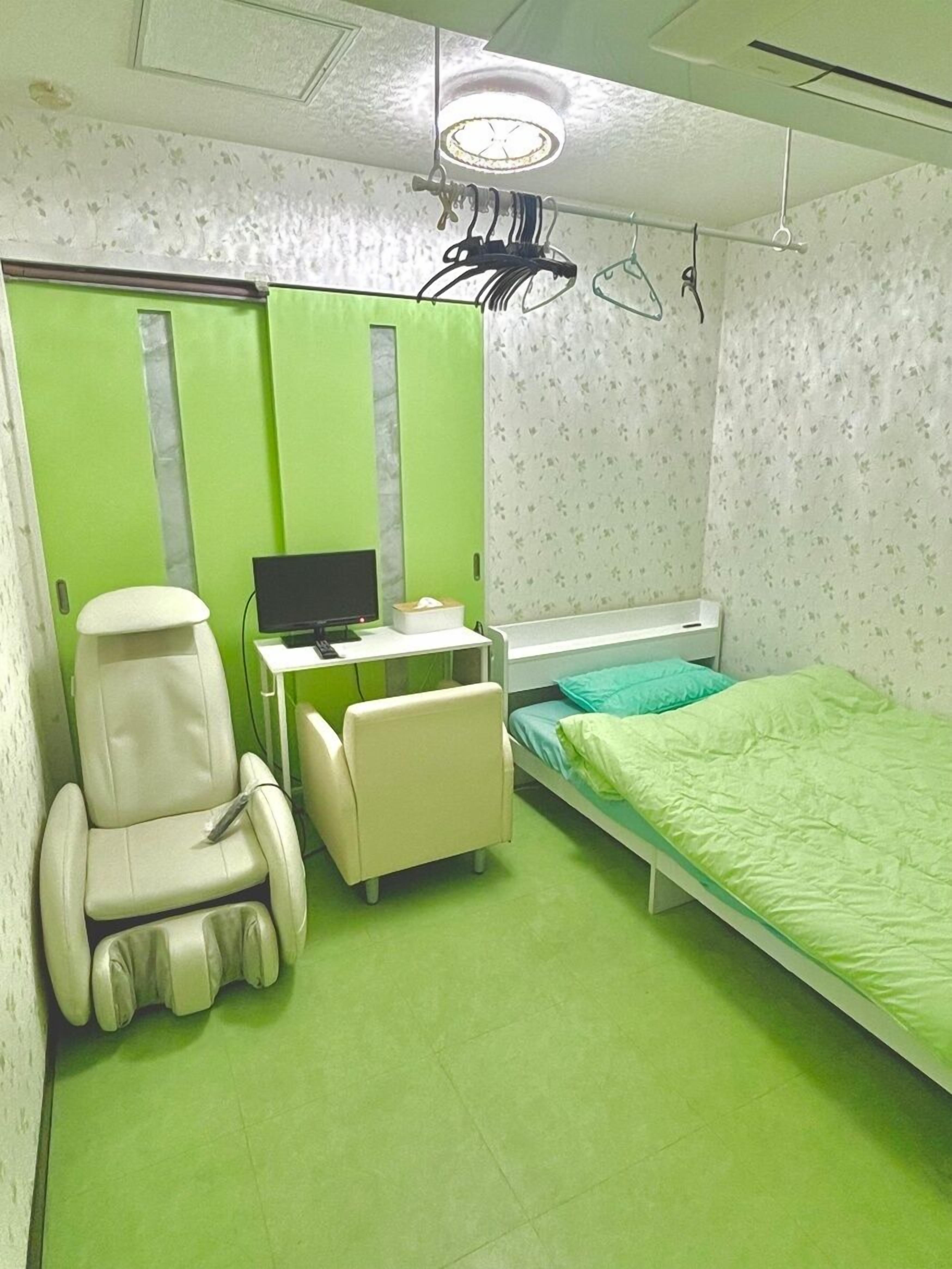A small, private room with a bed, a desk with a computer, a chair, and a small table with a tissue box.