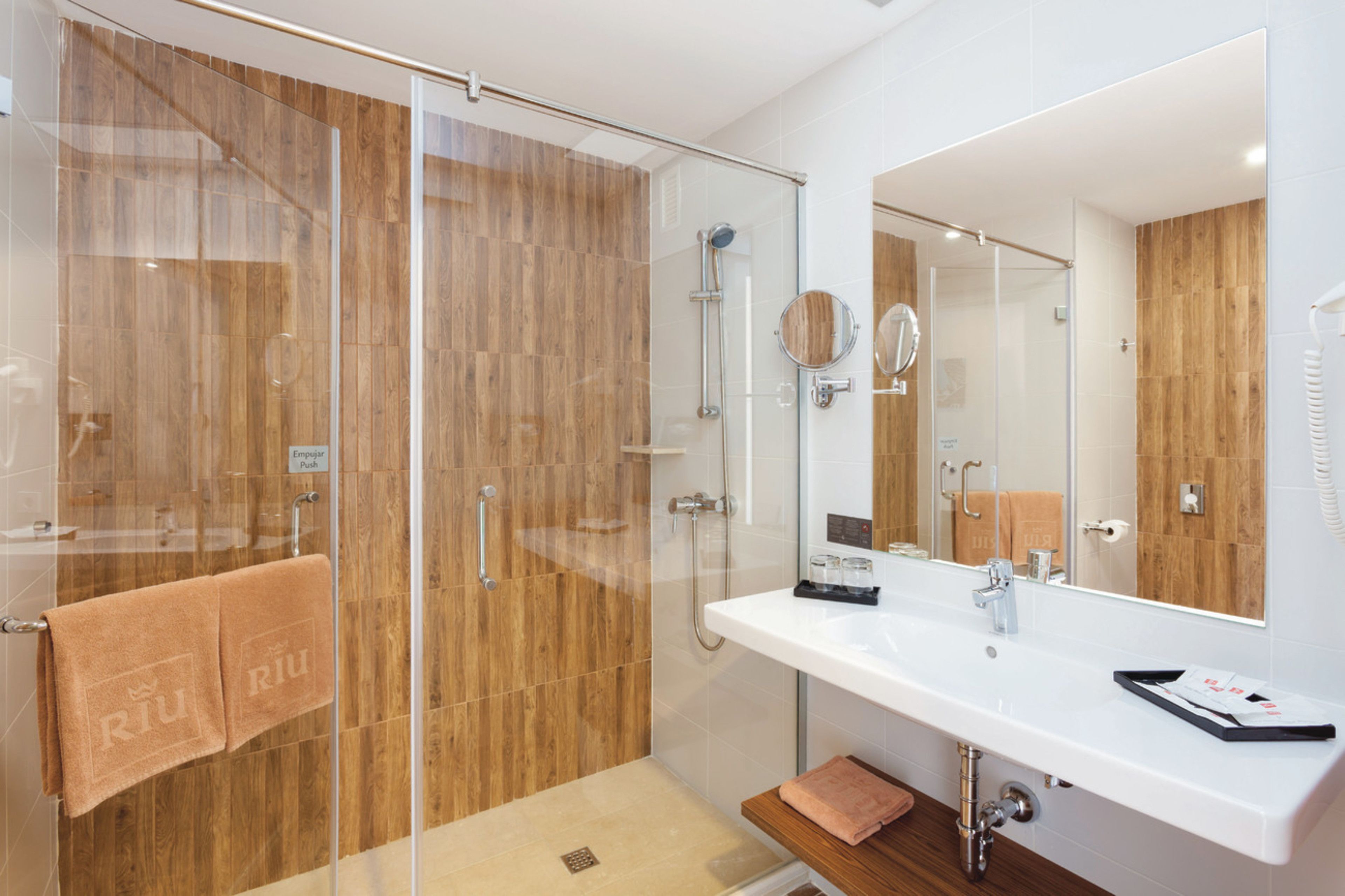 Une salle de bain moderne avec une douche à parois de verre, un lambris en bois, un lavabo blanc et un grand miroir.