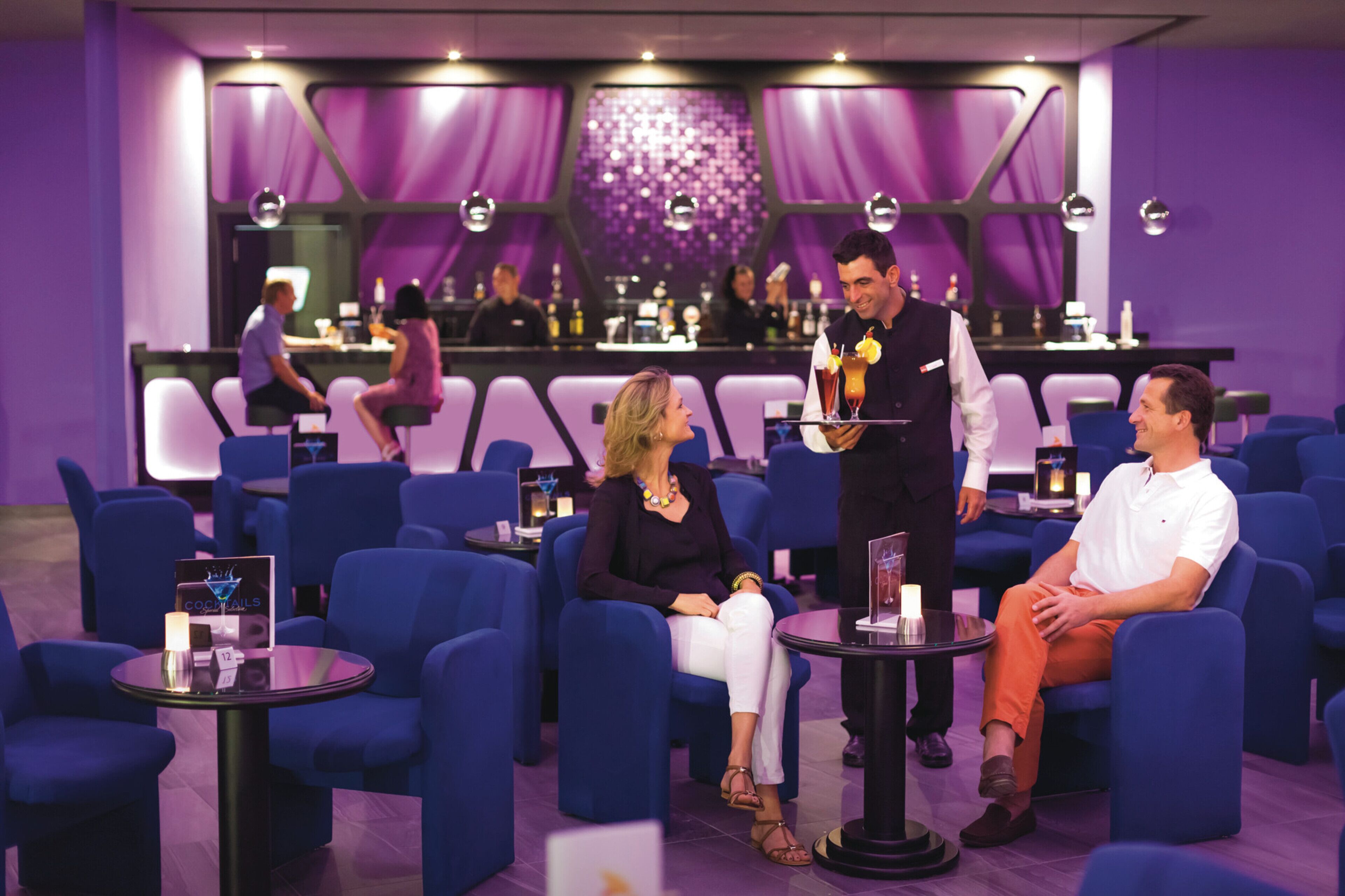 A bar area with blue seating, a bartender, and a bar counter with various items.
