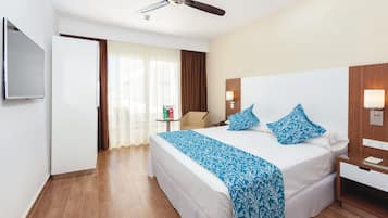 Una habitación de hotel con cama, ventilador de techo, televisor, mesita de noche y velador.