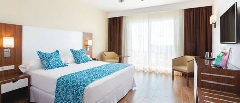 Una habitación de hotel con una cama grande, un escritorio, una silla, un ventilador de techo y un televisor.