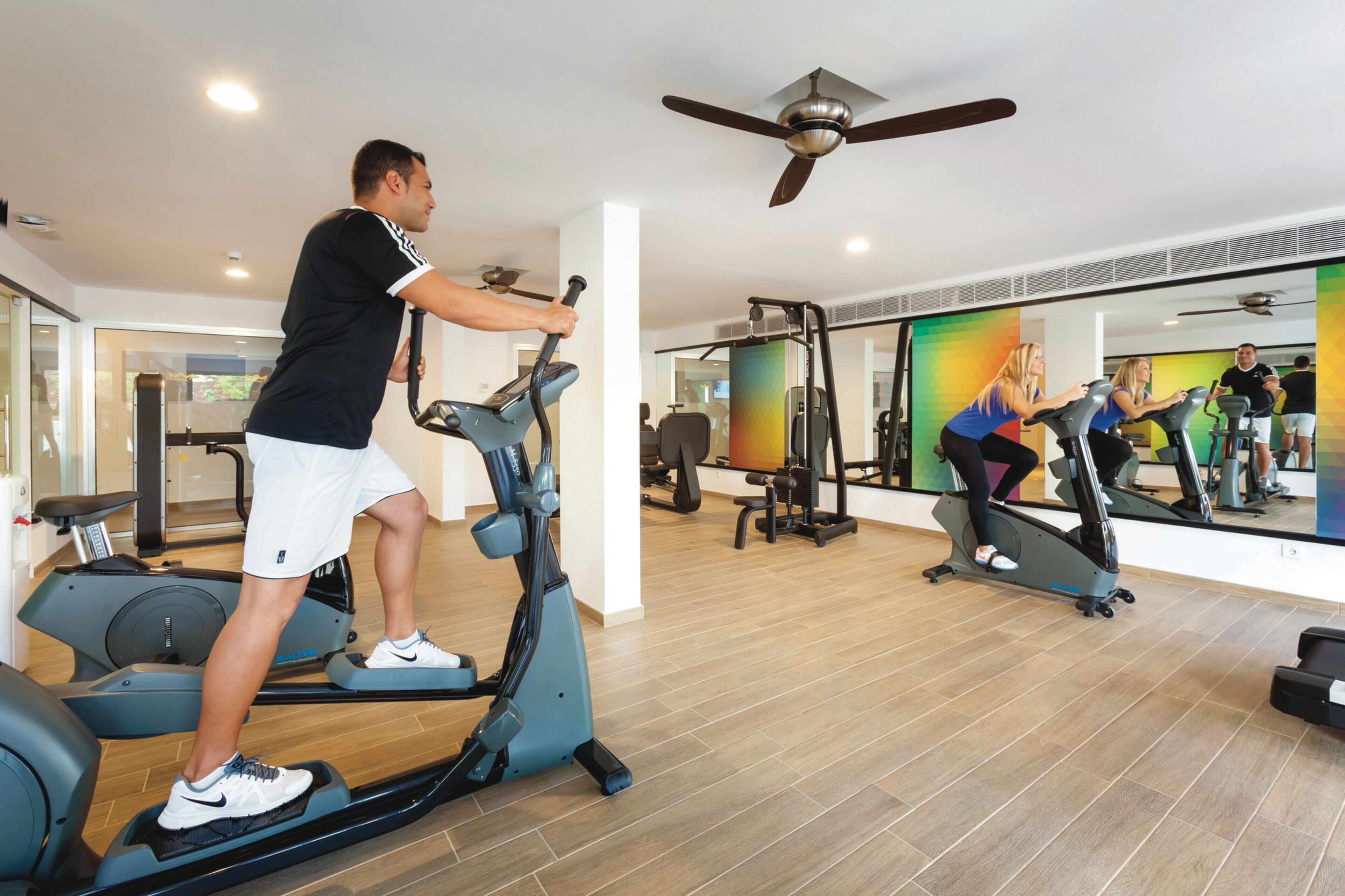 A gym with exercise equipment, a ceiling fan, and a large mirror reflecting the space.