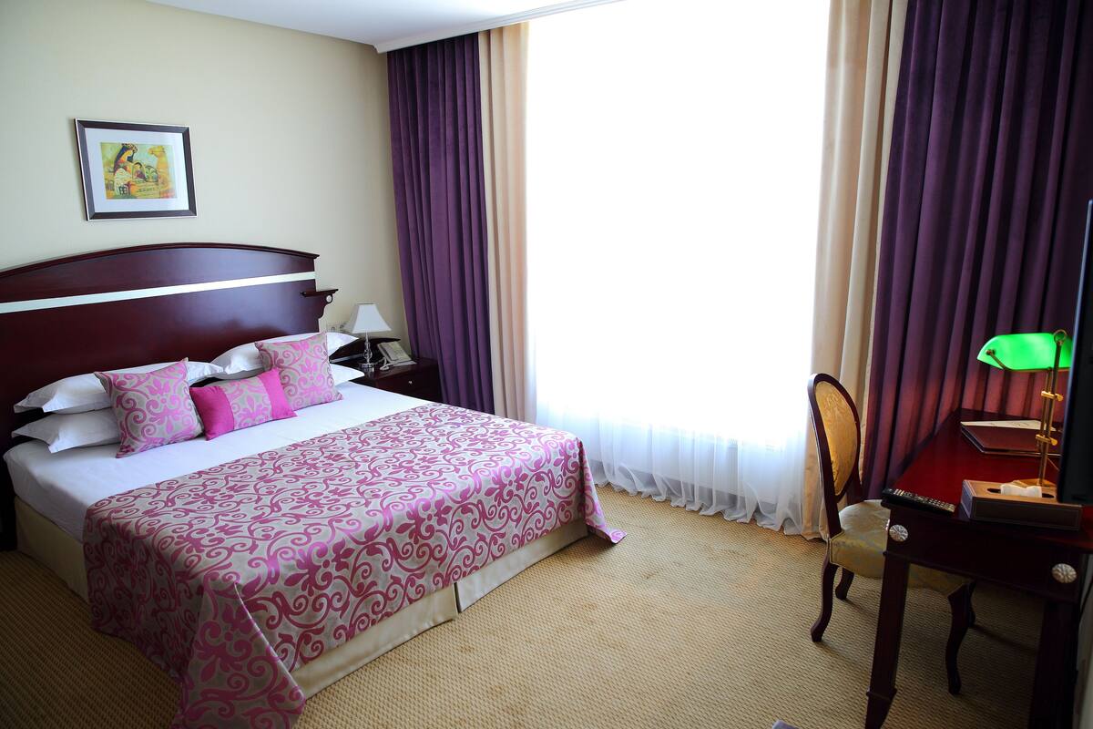 Una habitación de hotel con una cama grande, un escritorio con lámpara y una silla.
