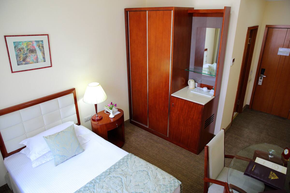 Una habitación de hotel con cama, mesita de noche con lámpara, armario, baño con espejo y una pequeña mesa con artículos de aseo.