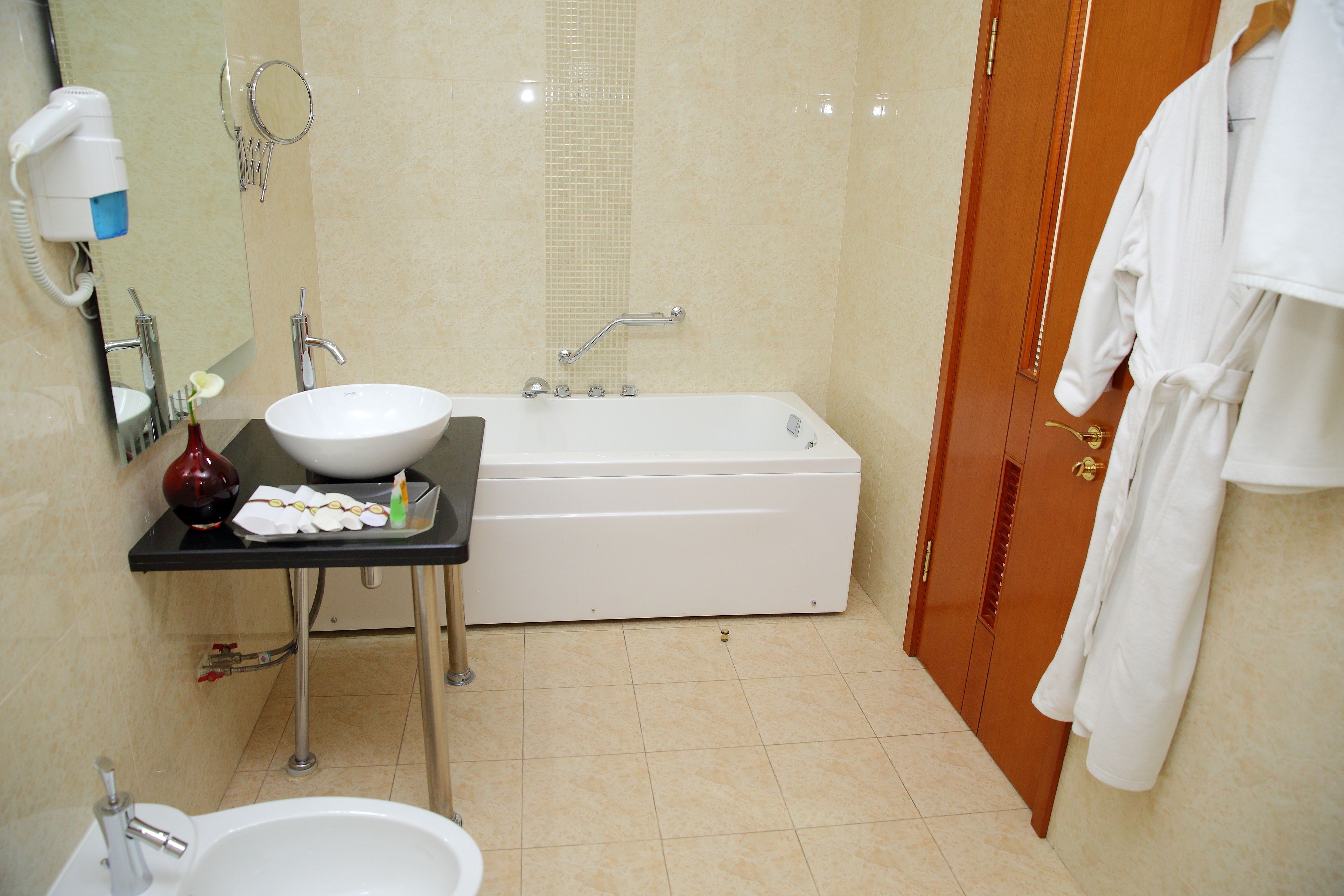 A bathroom with a sink, mirror, hairdryer, and a bathtub.