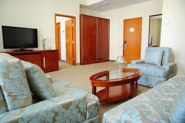 A living room with a flat-screen TV, two patterned sofas, a glass-top coffee table, and a wooden cabinet. - Park Hotel Bishkek (Bishkek)