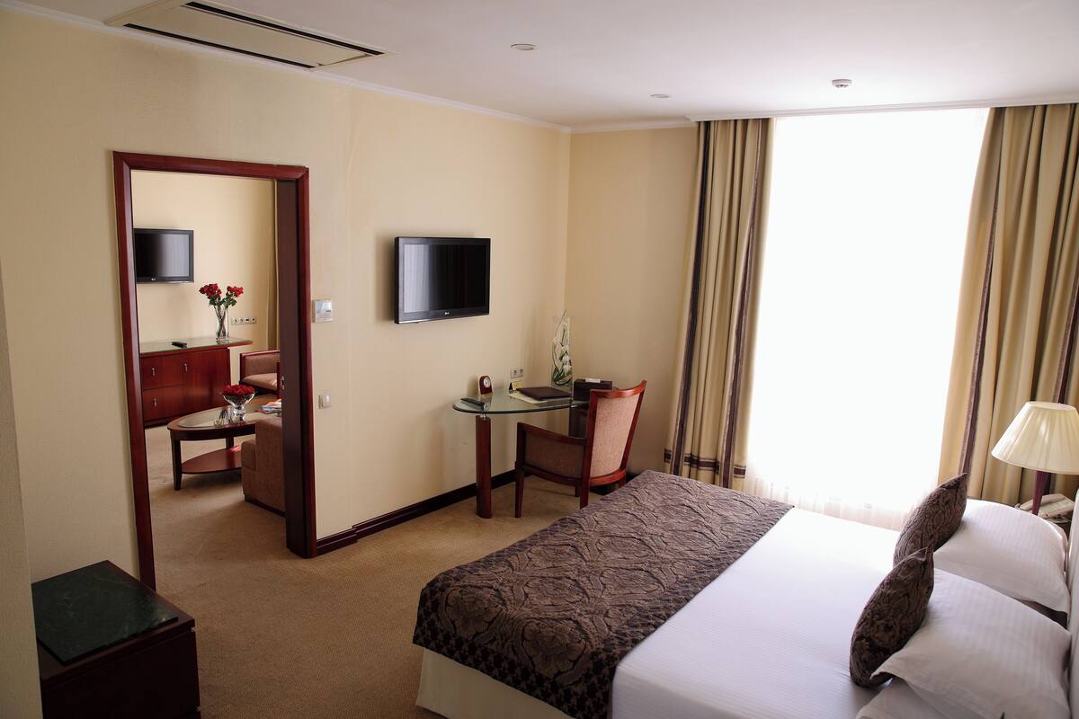 Habitación de hotel con cama, escritorio con silla, televisor y ventana con cortinas.