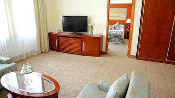 A living room with a television on a wooden cabinet, a glass coffee table, and a sofa with patterned cushions.