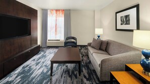 A hotel room with a flat-screen TV, a sofa, a coffee table, a lamp, and a framed picture on the wall. - Fairfield Inn & Suites by Marriott Denver Aurora / Parker (Aurora)
