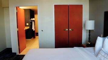 Una habitación de hotel con una cama grande, un armario, una mesita de noche con lámpara y un baño visible a través de una puerta abierta.