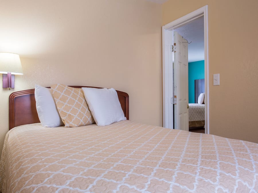 Une chambre à coucher comprenant un lit, une table de chevet, une lampe et une porte donnant sur une autre pièce.