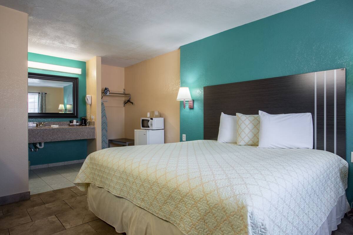 A hotel room with a large bed, a bathroom with a sink and mirror, and a microwave on a small table.