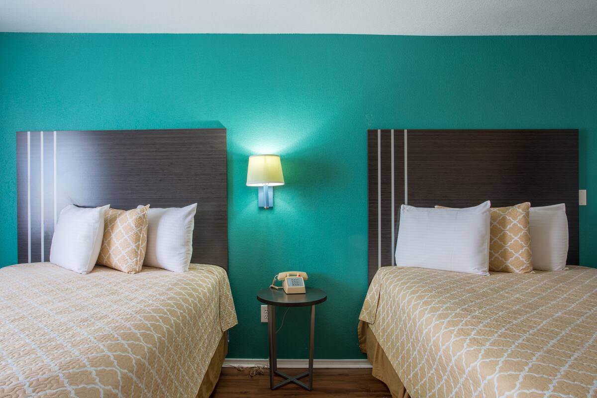 A hotel room with two beds, a small table with a lamp, and a telephone.