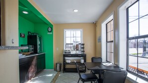 A compact kitchen with a green accent wall, a window with blinds, a sink, and a countertop with a microwave. - Pinn Road Inn and Suites (San Antonio)