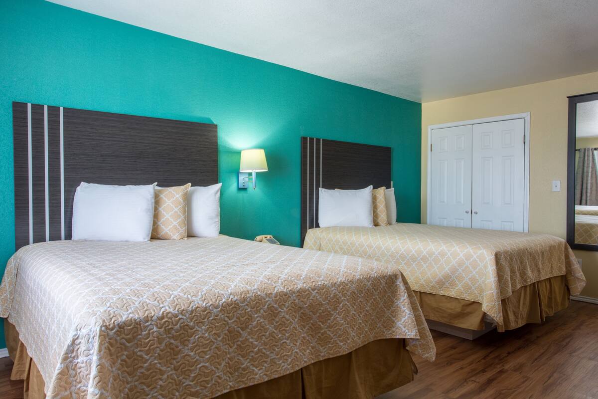 A hotel room with two beds, teal walls, and wooden flooring.