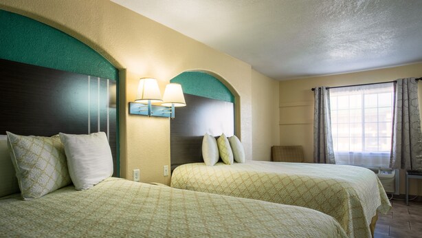 A hotel room with two beds, a nightstand, a lamp, and a window with curtains. - Pinn Road Inn and Suites (San Antonio)
