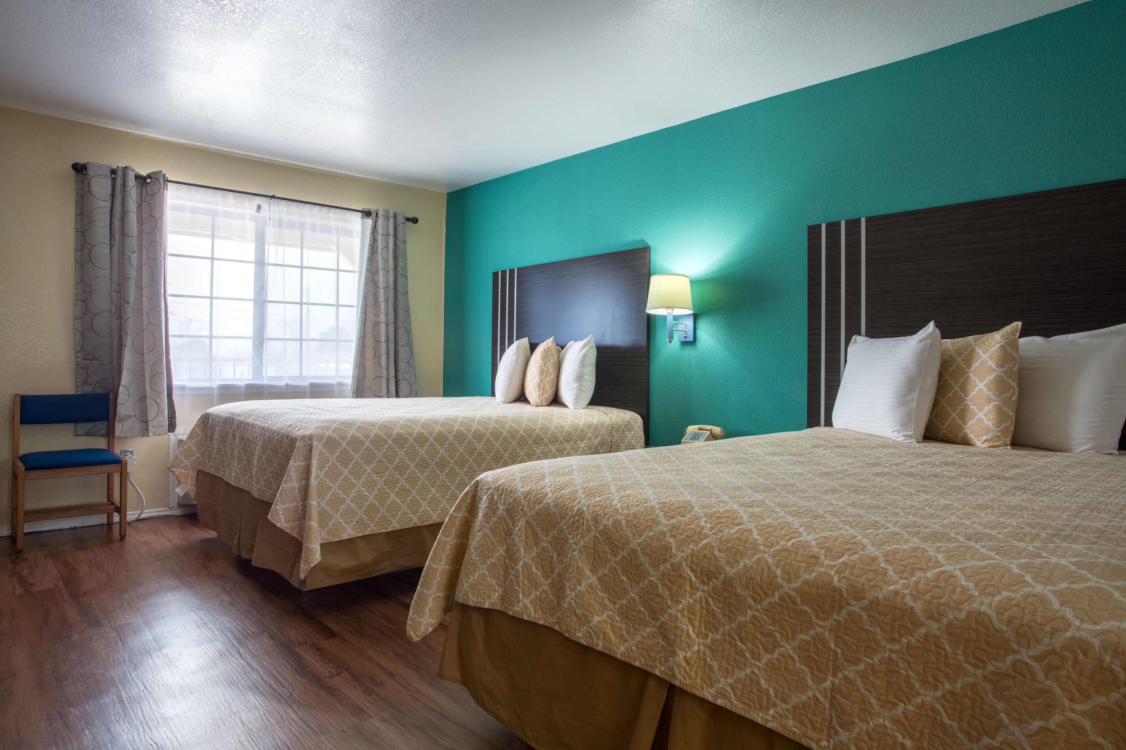 Habitación de hotel con dos camas, una silla, un ventanal con cortinas y una lámpara de pared.