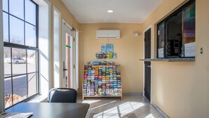 A hotel lobby with a reception desk, a magazine rack, and a large window offering a view of the parking lot. - Pinn Road Inn and Suites (San Antonio)