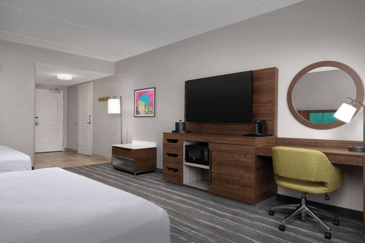 Ein Hotelzimmer mit einem Bett, einem Schreibtisch mit Computer, einer Mikrowelle, einem Fernseher und einem Spiegel.