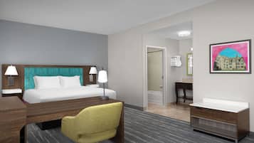Ein Hotelzimmer mit Bett, Nachttischen, Schreibtisch, Stuhl, Schminktisch und einem gerahmten Bild an der Wand.