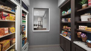 A narrow hallway with shelves stocked with snacks and beverages, leading to a room with a desk and chair.